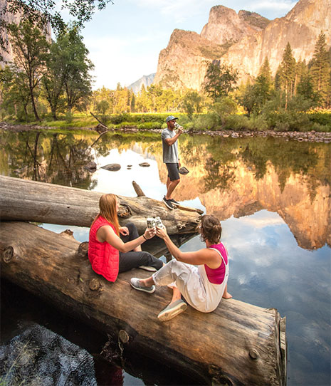 People sitting on large log by a lake